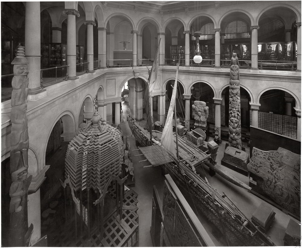 Image: Black and white photograph of a museum space with several objects, among them a large totem pole.